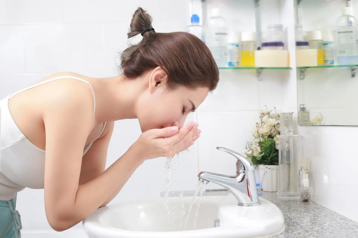woman splashing water on her face above a sink