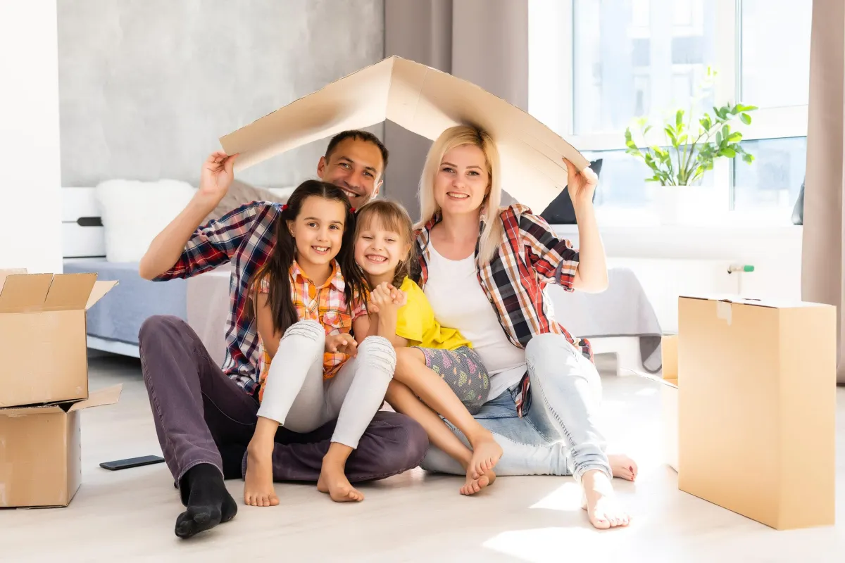 family sitting on floor holding a flat box over their head