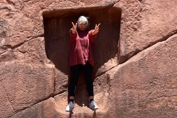 Woman standing in a carved stone alcove with arms extended forward, representing a grounded moment of return and embodied presence.