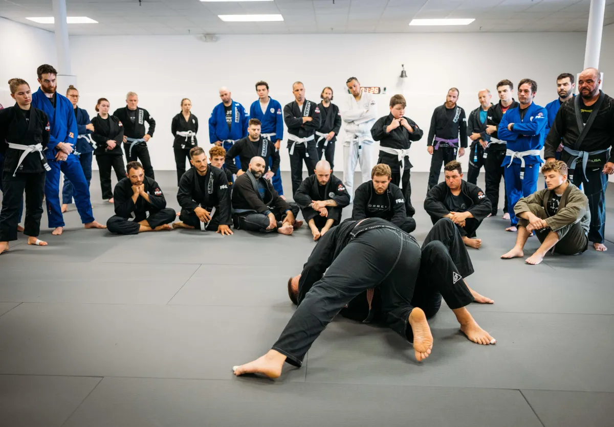 A Brazilian Jiu-Jitsu students training on mats, mid-drill, wearing gis and sweating during intense practice.