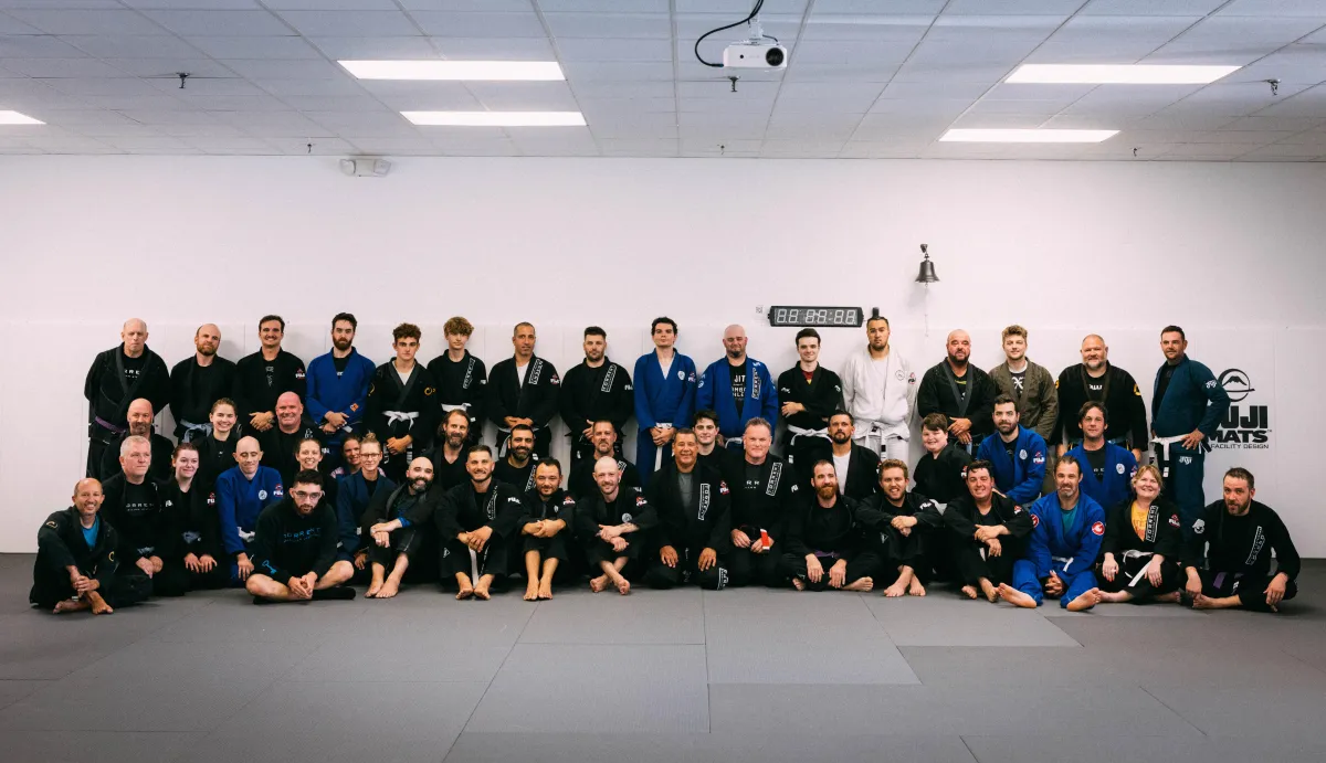A group photo of adults at Torrent Brazilian Jiu-Jitsu, smiling and posing together after a class, showcasing the supportive team atmosphere.
