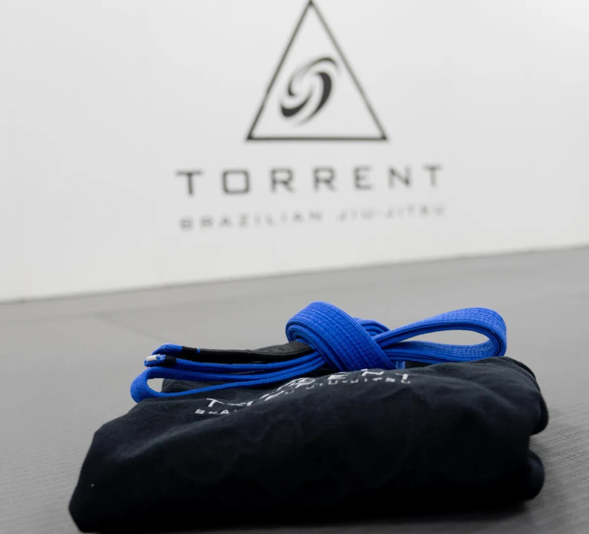 A Brazilian Jiu-Jitsu gi with a blue belt, featuring the Torrent Brazilian Jiu-Jitsu logo on the back.
