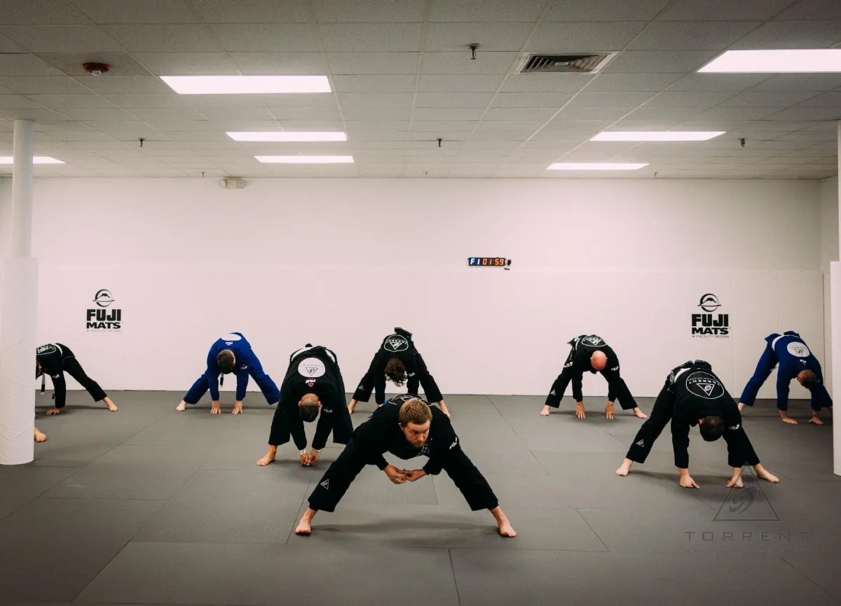 Students stretching and doing mobility drills in a Brazilian Jiu-Jitsu gym environment