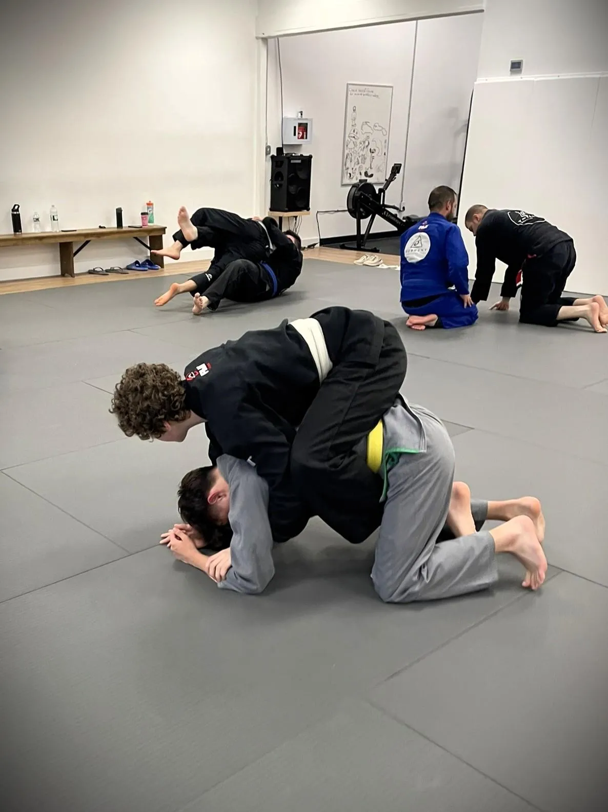 Two Brazilian Jiu-Jitsu students grappling on the mat during training, wearing traditional gis and engaged in a close-contact position.