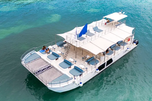 Un catamarán navegando al atardecer en aguas cristalinas, con personas relajadas en la cubierta.