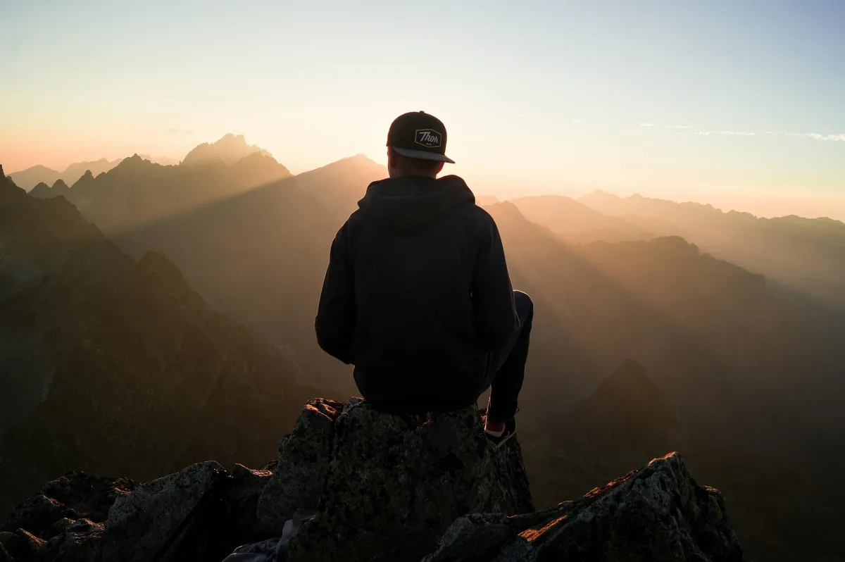 Person on mountain peak at sunrise, symbolizing new beginnings.