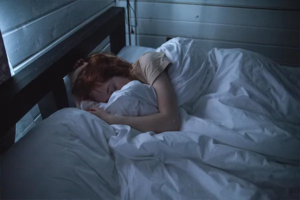 A woman peacefully asleep in bed, representing restful sleep and the benefits of healthy sleep hygiene.