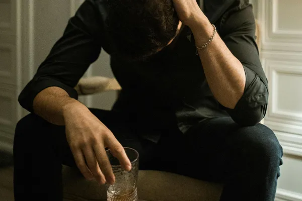 Person holding an alcoholic drink while looking anxious.