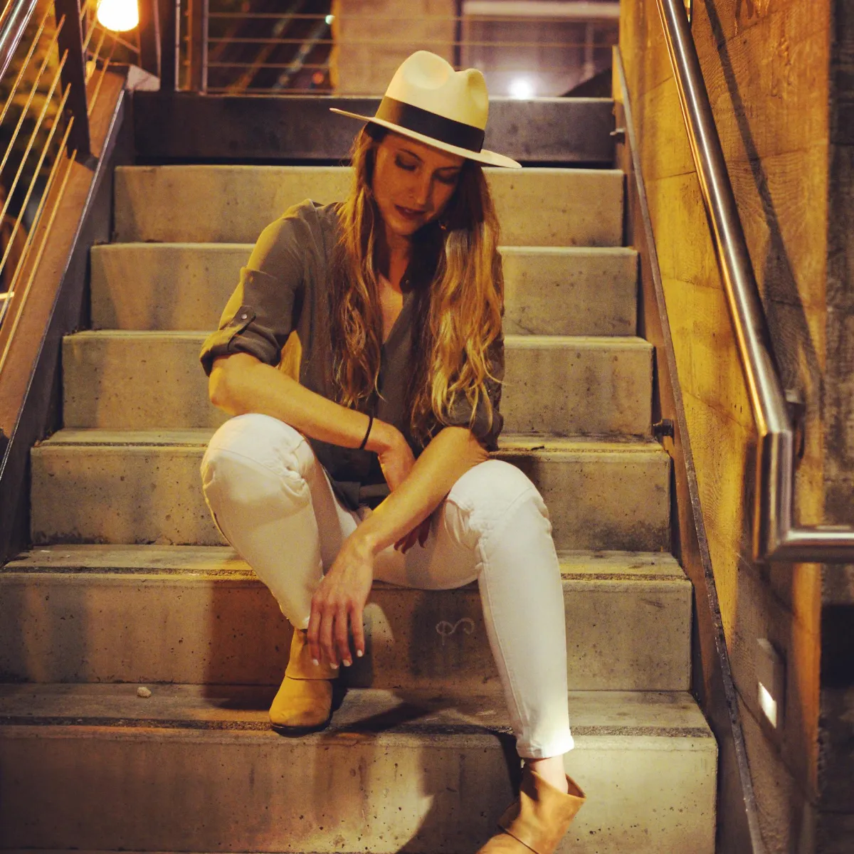 Woman in a hat is sitting on the stairs looking down.