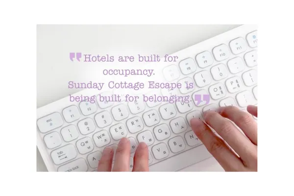 Close-up of a woman’s hands typing on a white keyboard with the blog title “Hotels Are Built for Occupancy – Sunday Cottage Escape Is Built for Belonging” displayed on screen.