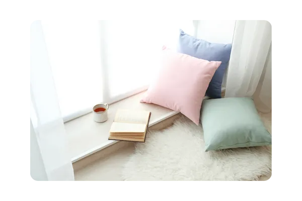 A bright, serene window nook with pastel throw pillows and soft light — capturing the heart of calm and relaxation at Sunday Cottage Escape, where every detail is designed for peace.
