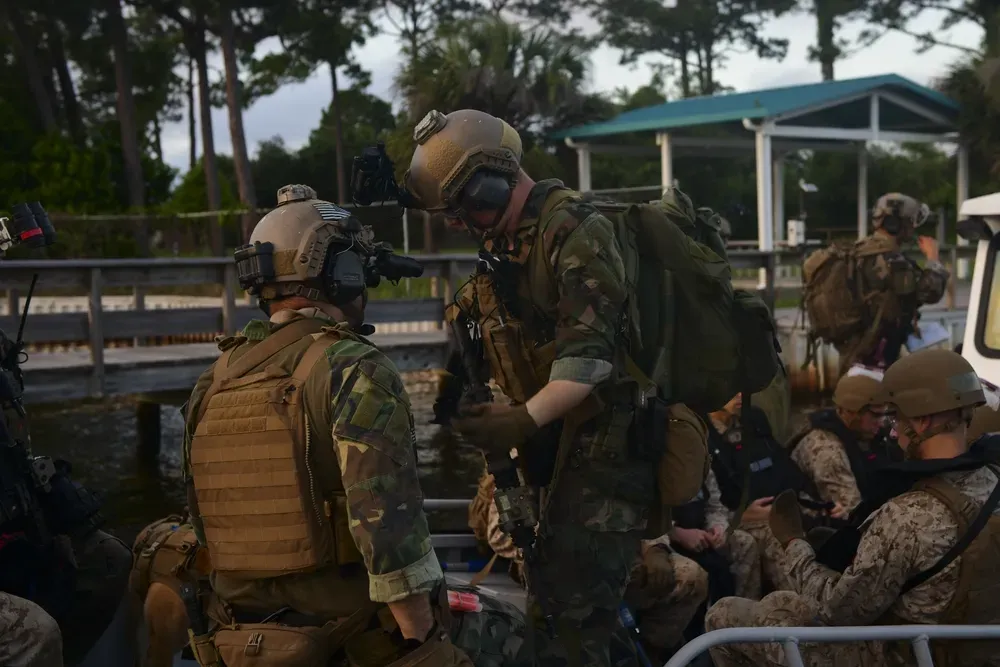 soldiers in full combat gear working outside in a boat at a dock during the day