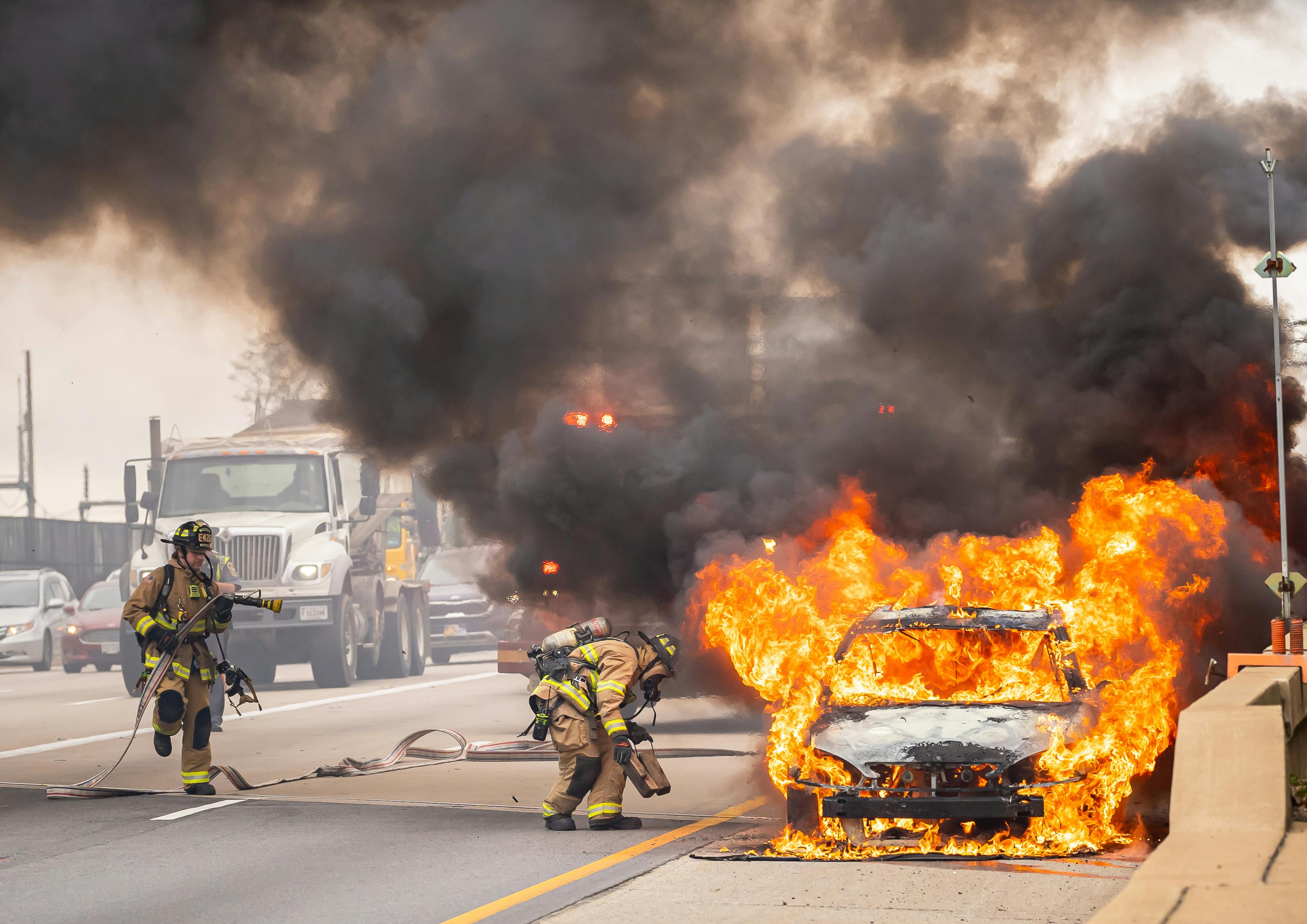 firefighters putting out a car fire in the middle of a street