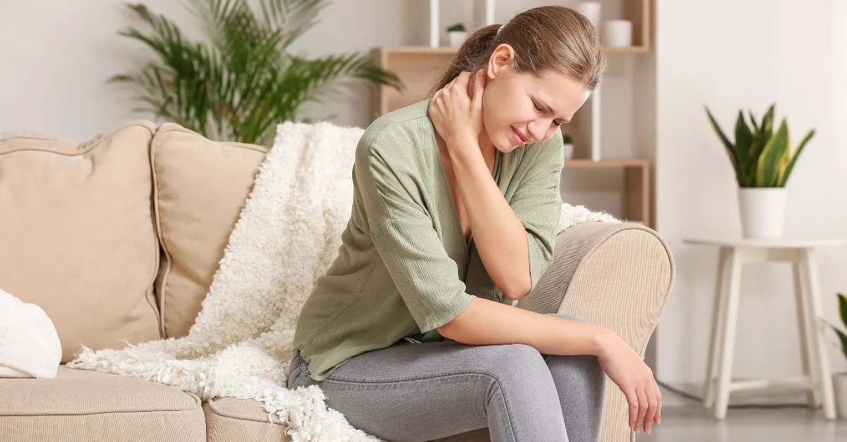 Woman on couch clutching neck in pain