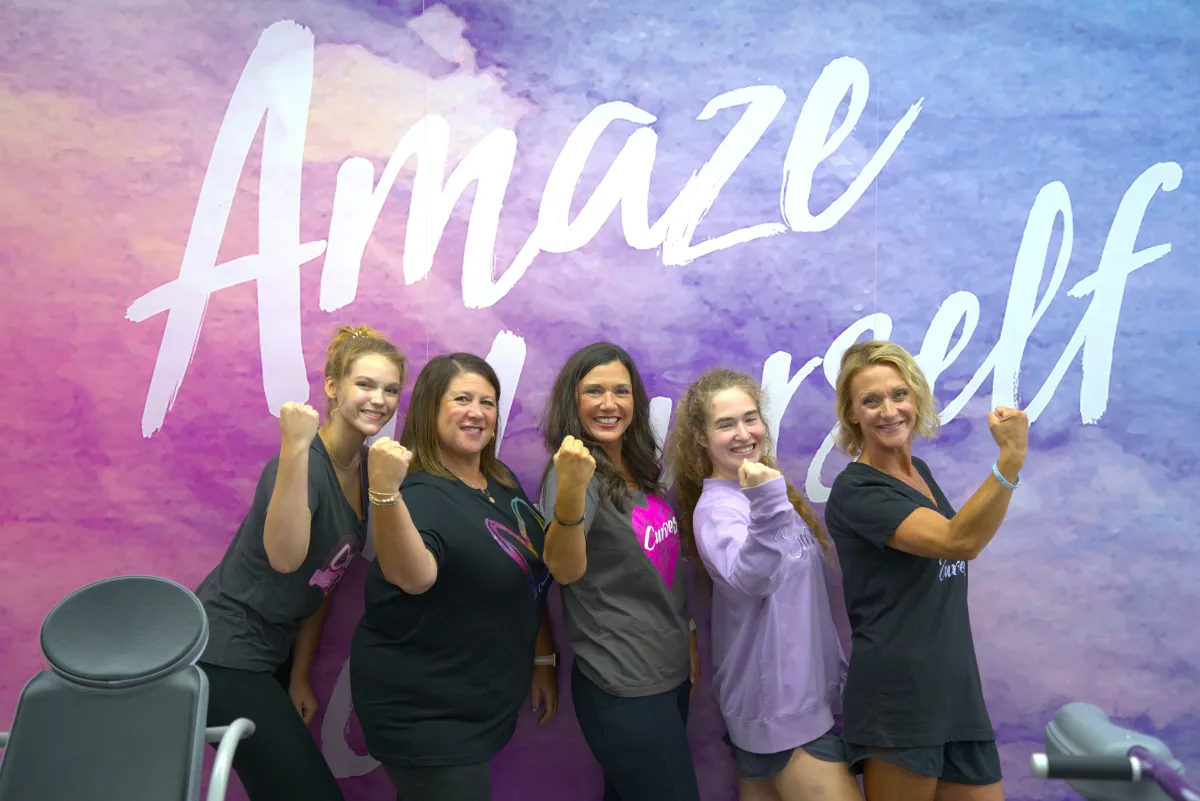 Women at Curves in Front of Amaze Yourself Sign