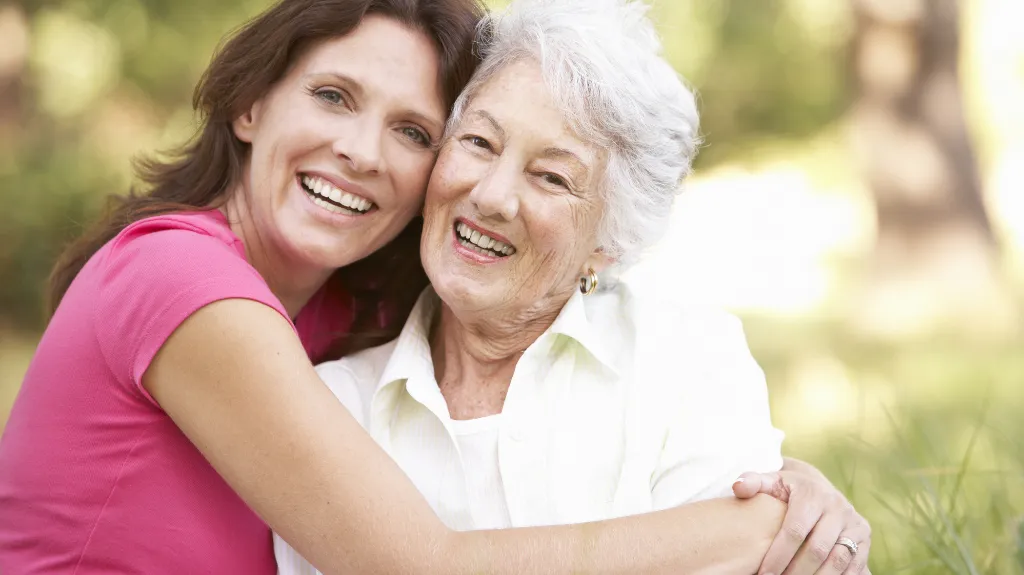 Smiling senior hugging caregiver outdoors.