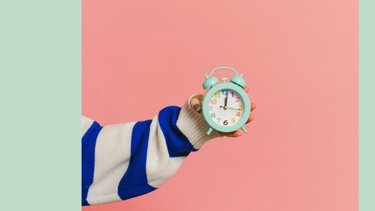 A women's arm holding a clock representing passing time or decisions deferred.