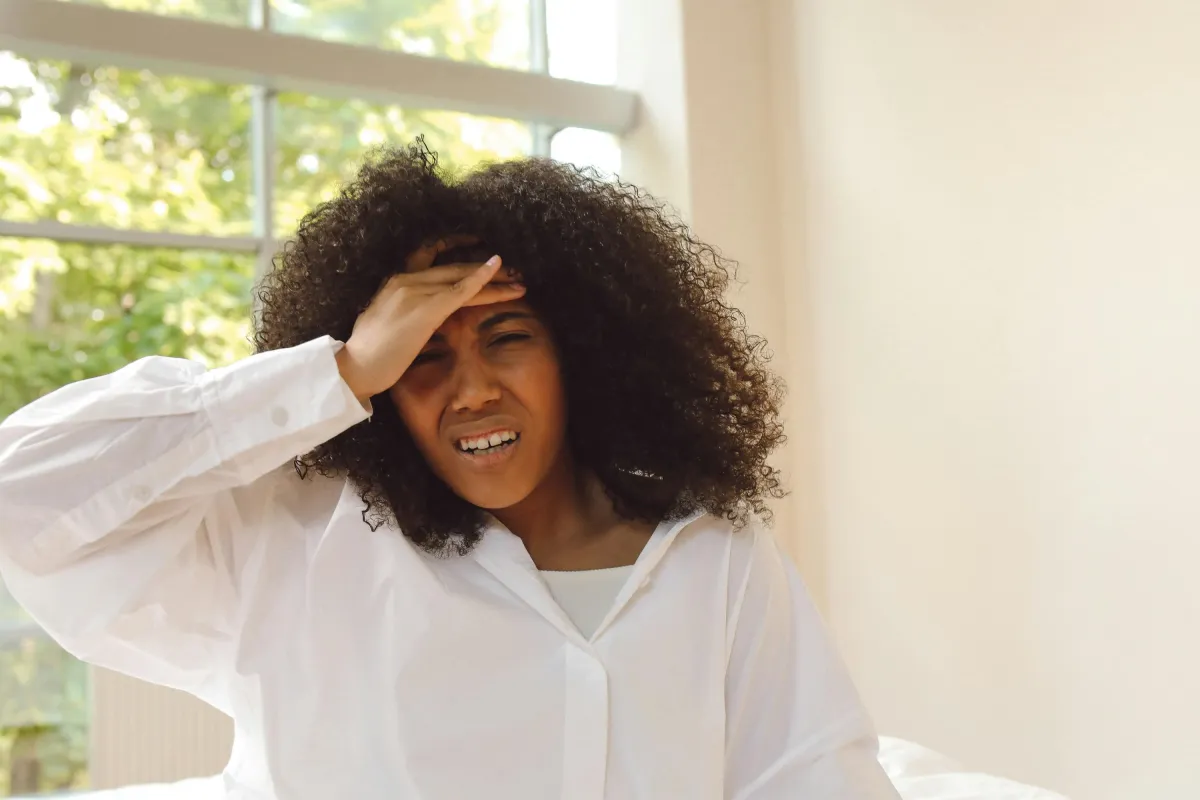 Woman in a white blouse holding her forehead in discomfort, expressing the struggle of chronic pain and its impact on daily life.
