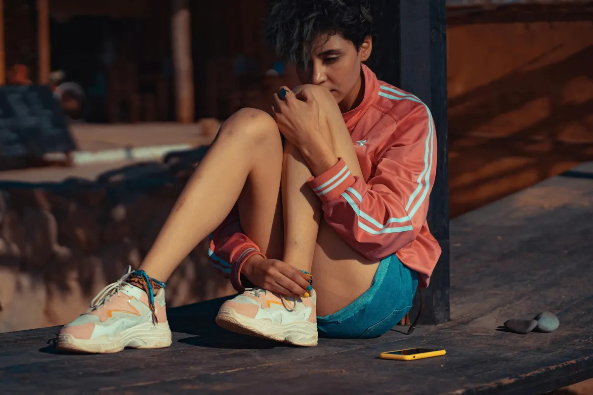 A young athlete in sportswear sits alone outdoors, looking down with a pensive, distressed expression, reflecting the mental health struggles many youth athletes face.