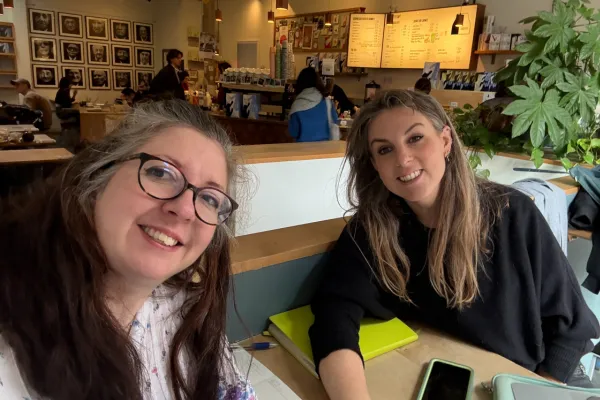 two women seated at a cafe table looking at the camera
