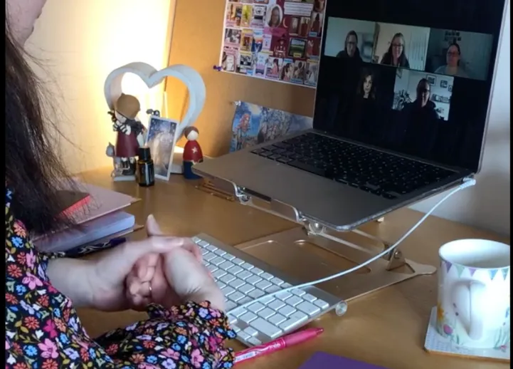 Woman at desk looking at computer screen which displays an online meeting