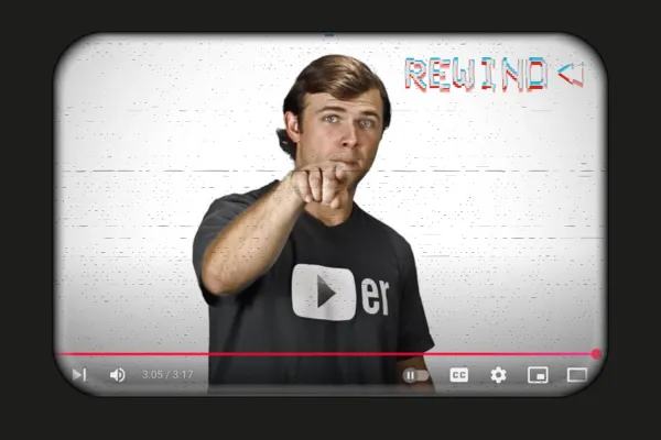 A paused YouTube video showing Jake Larsen, founder of video power marketing, pointing directly at the camera. He is wearing a black t-shirt with a partially visible YouTube-style logo. The screen has a retro VHS-style distortion effect, and the word "REWIND" appears in a glitchy, blue-and-red font in the upper right corner.