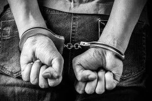 Black and white image of a person in handcuffs with hands behind their back.