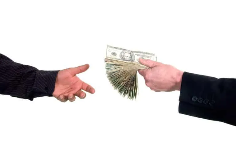 One person handing a large stack of U.S. dollar bills to another person.