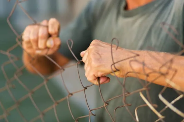 Person gripping and bending a wire fence with both hands.