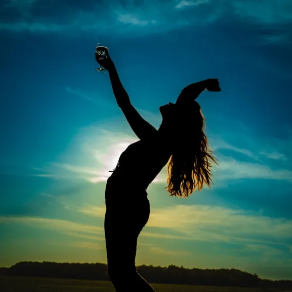 mujer a contraluz brindando al cielo en el atardecer
