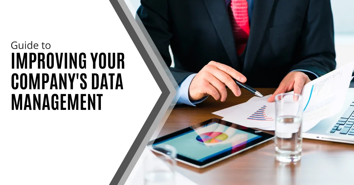 The image features a person in a business suit sitting at a desk, focusing on analyzing printed charts and graphs. In front of them are a tablet displaying colorful charts, a laptop, and a glass of water. The scene suggests a professional setting where data analysis and management are key tasks. The left side of the image includes the text: "Guide to Improving Your Company's Data Management" in bold, modern font. The overall composition emphasizes the importance of effective data management in a business environment.