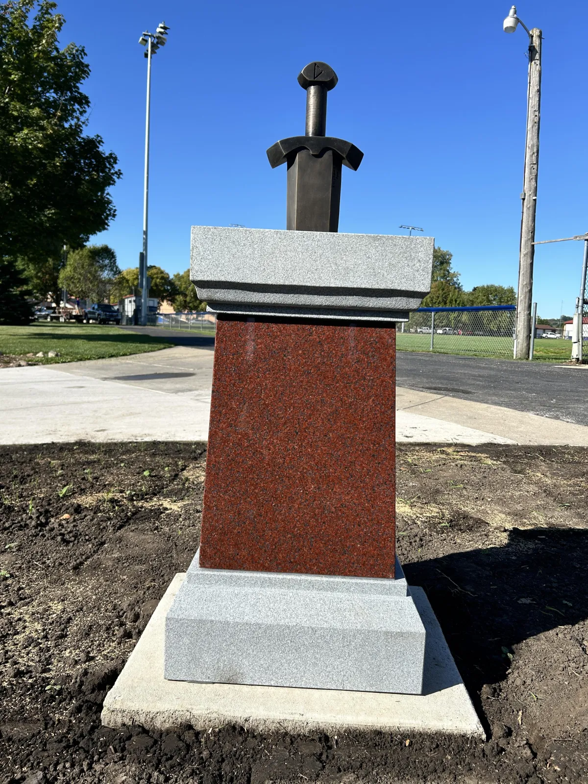 a stone monument with bronze sword sticking out the top of it