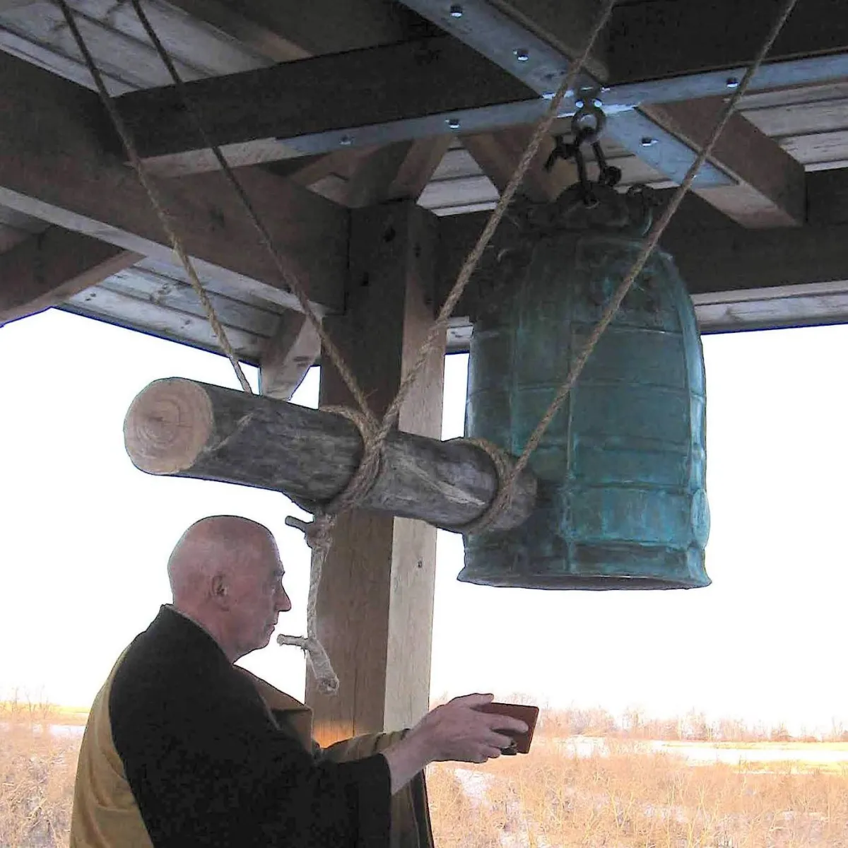 custom bronze bell hangs in an open outdoor shelter with a traditional striking log