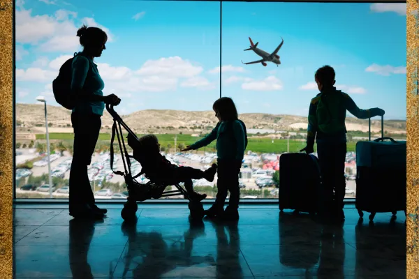 Silhouette image of Mom standing in airport window with a stroller and 2 bigger kids with luggage watching an airplane