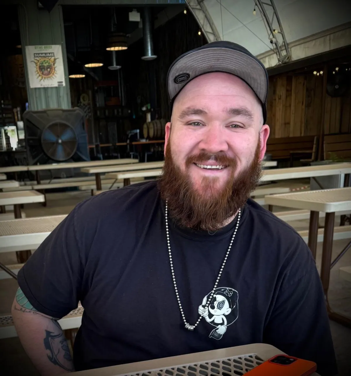 Photographer Jaymz Maurer smiling at a table, wearing a black shirt and cap, featured artist at Create Gallery and Frames in Garden City, Idaho.