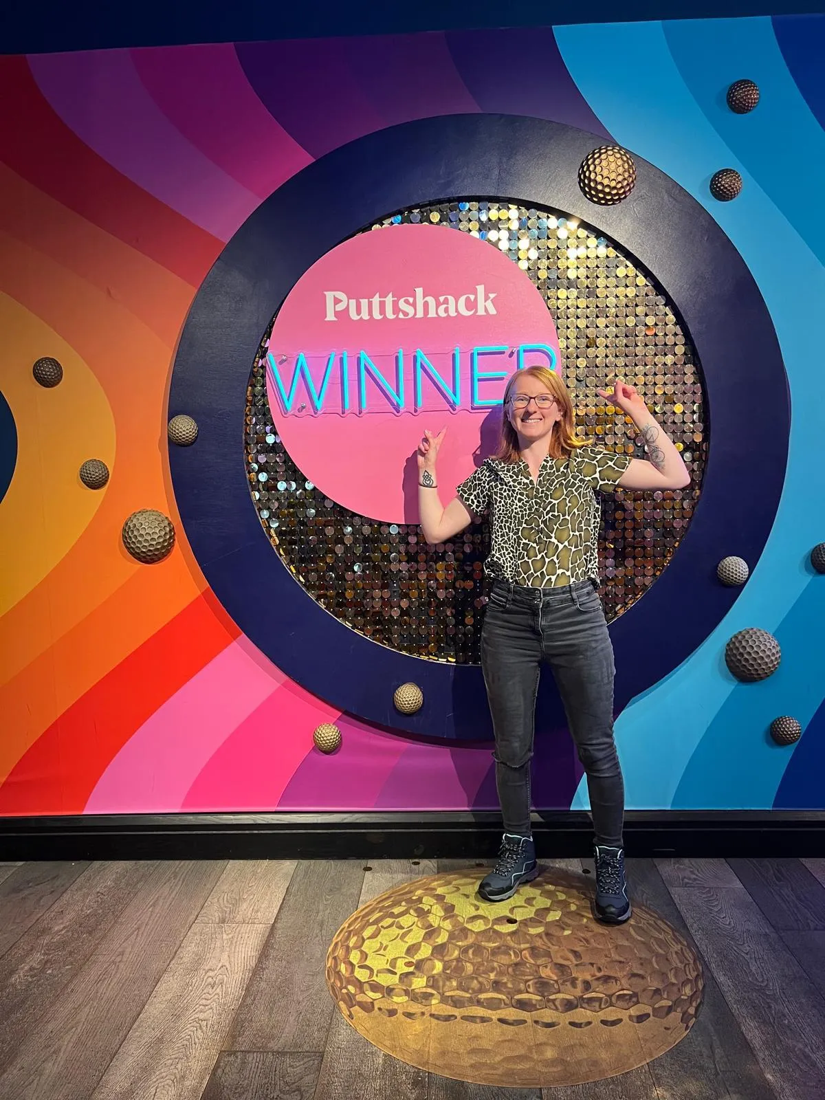 Woman smiling and posing in front of a colorful Puttshack Winner backdrop.