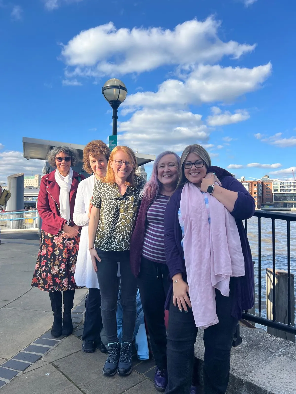 Group of women entrepreneurs standing together outdoors on a sunny day with a waterfront background.