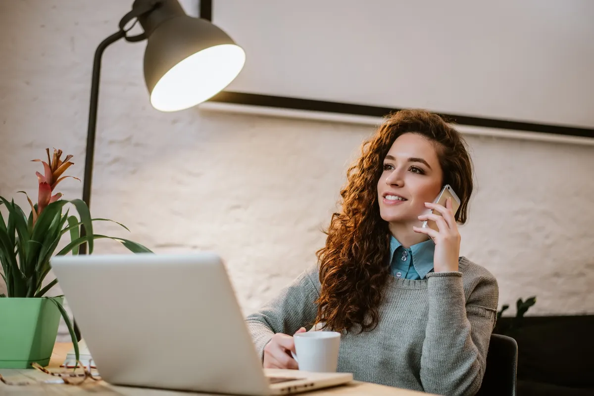 Businesswoman multitasking at her desk with a laptop and mobile phone discussing immediate callback solutions