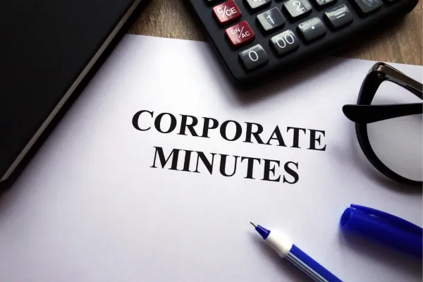 Image of corporate minutes on a desk with a calculator, eye glasses and a pen.