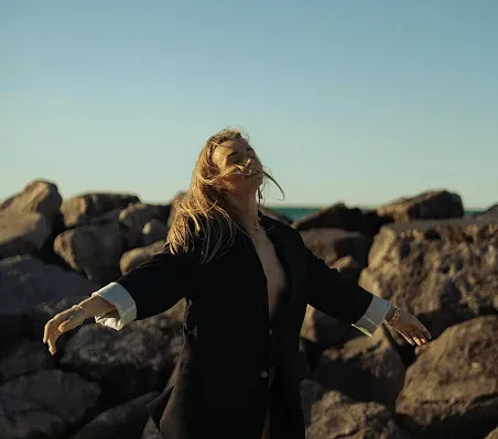 Woman with arms outstretched on a rocky beach at sunset.