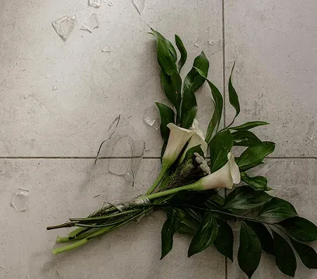 A broken glass vase and a wilting bouquet of white lilies on a cold tile floor, symbolizing the emotional and financial fragility of a family separation.
