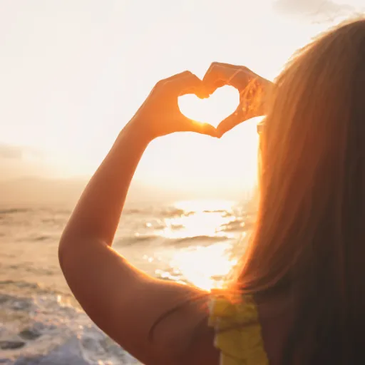 Woman forming a heart with her hands in the sunlight — symbol of self-love, healing, and emotional transformation.