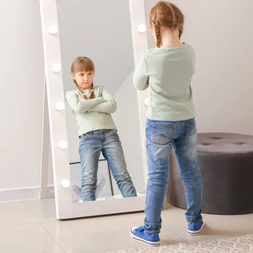 A young girl stands in front of a mirror with an angry expression, struggling with hurt and rejection, symbolizing childhood emotional pain and healing.