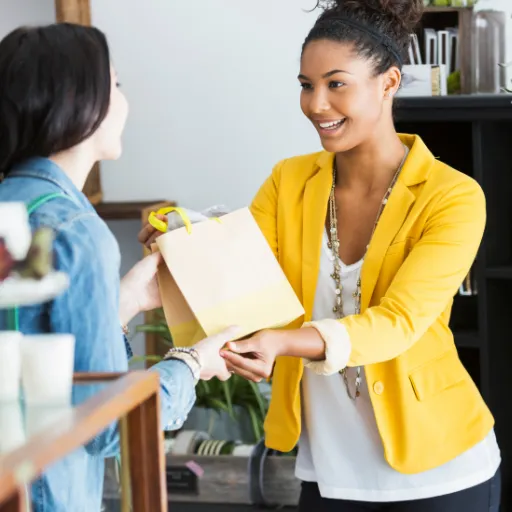 Woman handing a small brown bag to another woman, symbolizing support, generosity, and the act of receiving.