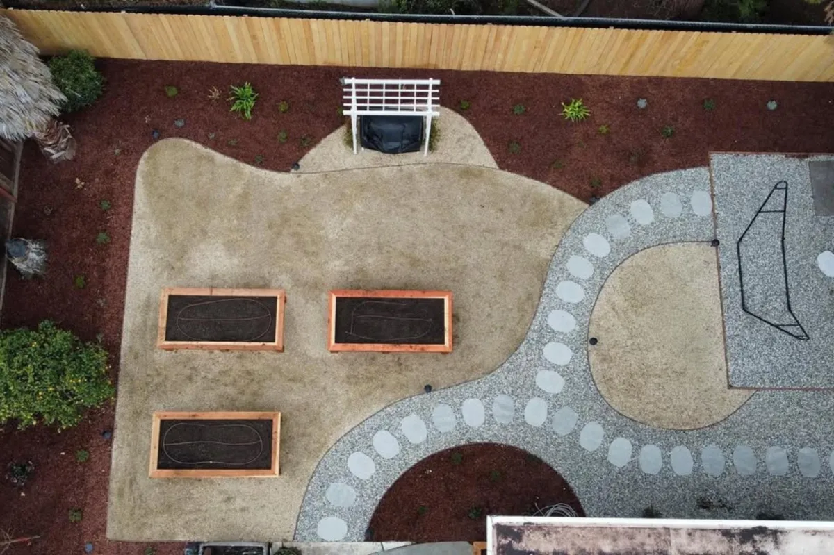 Aerial view of a backyard featuring a well-maintained garden bed surrounded by lush greenery and landscaping elements.