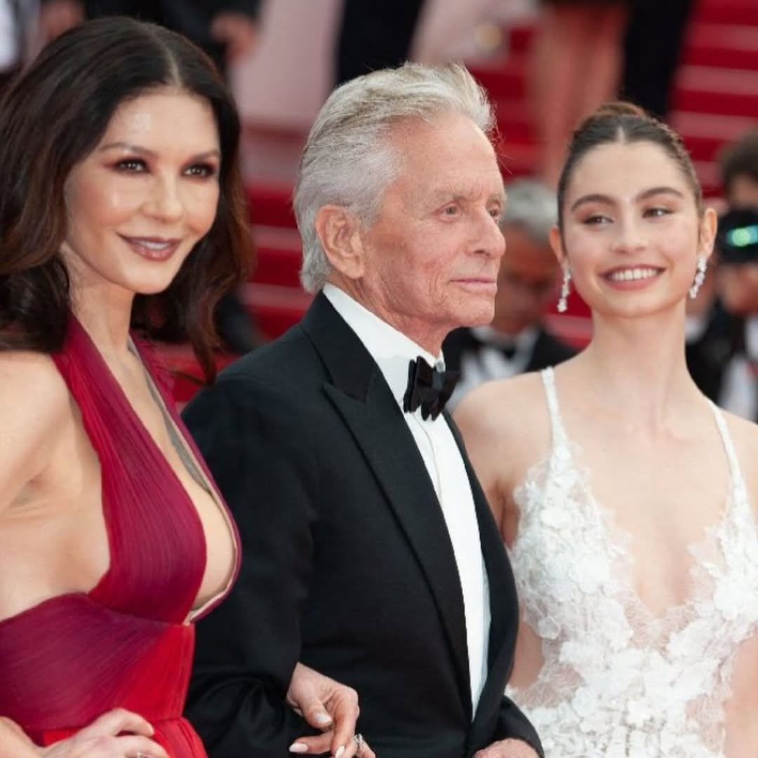 Catherine Zeta-Jones smiling at the Las Vegas Formula 1 Grand Prix wearing a black-and-white monochrome outfit, standing next to husband Michael Douglas and son Dylan.