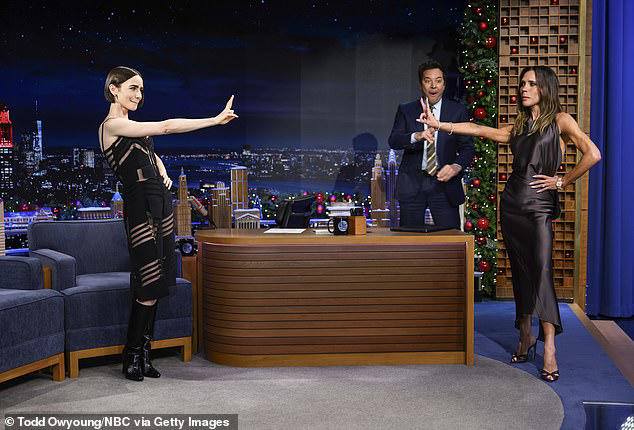 Victoria Beckham poses in a sleeveless charcoal satin dress inside the Tonight Show backstage room, showing toned legs and glowing skin while preparing for her appearance.