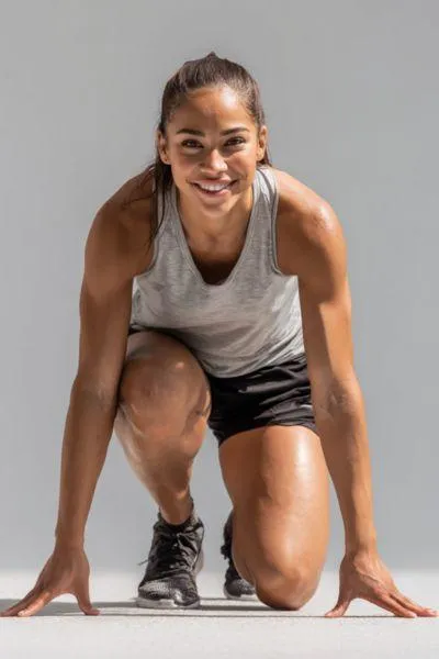 Smiling female athlete in starting position, embodying self-belief, preparation, and a growth mindset as foundations of internal confidence in sports