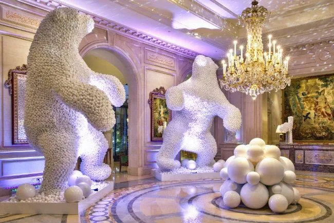 Hotel banquet hall decorated for Christmas with grand trees, shimmering lights, floral centerpieces, and festive accents.