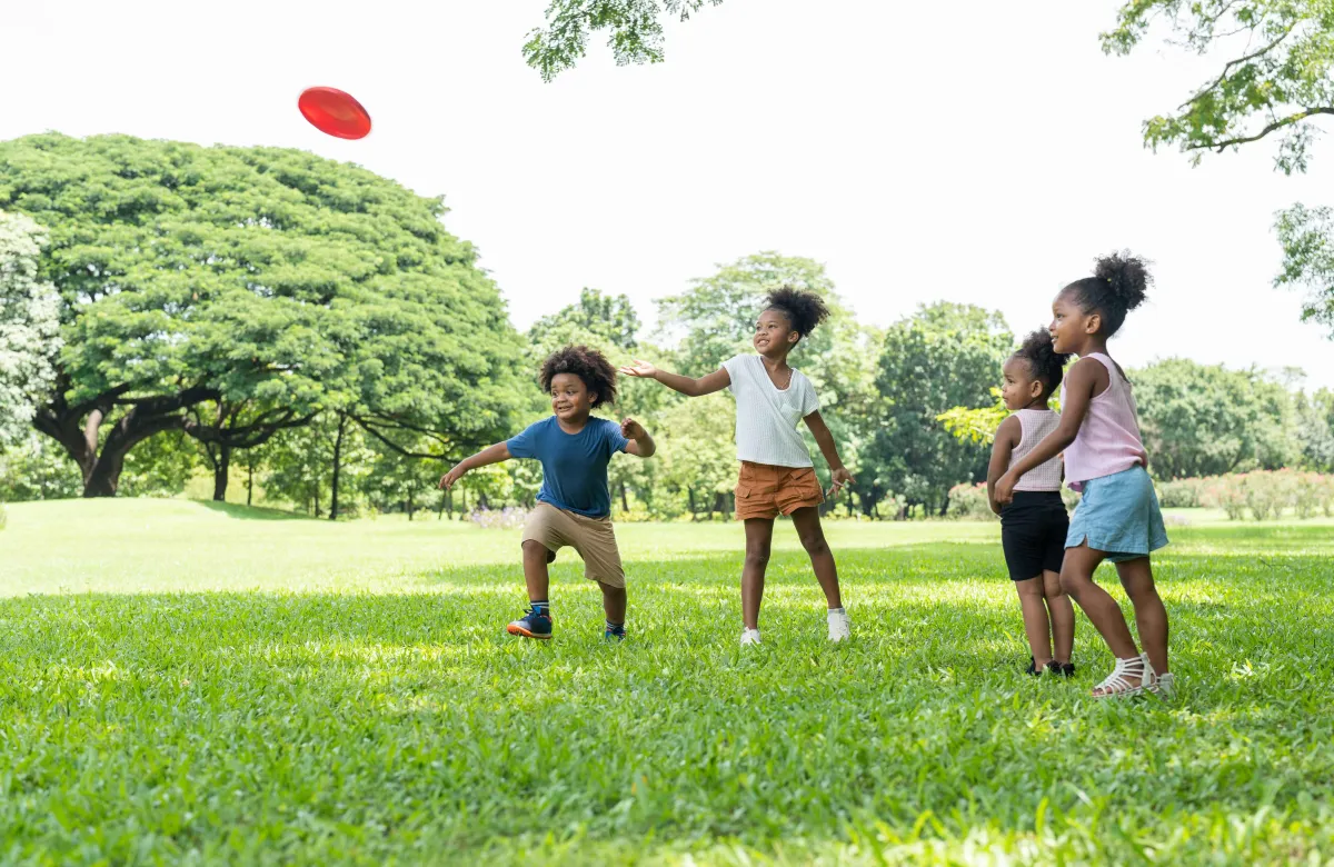 A group of children joyfully play together in a park, tossing a frisbee and building social skills through teamwork and laughter.